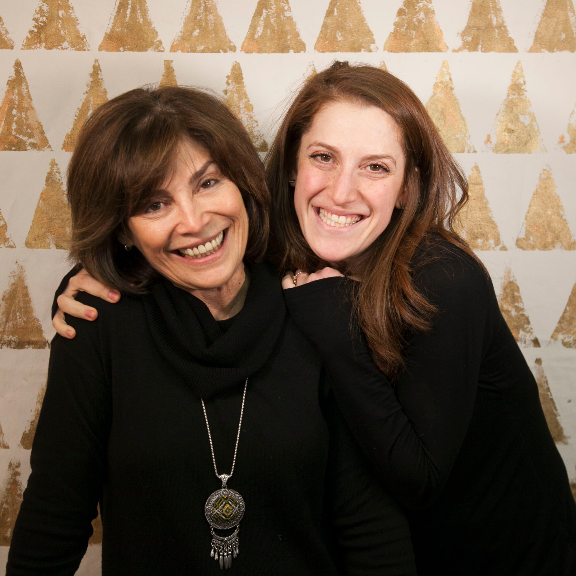 Jill and Jackie with their heads together, smiling at the camera in front of their gold triangle mural